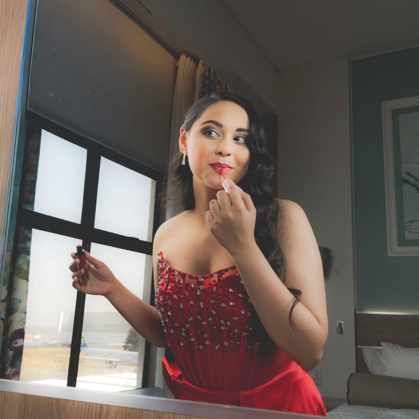 Beauty portrait: model in a red gown applying lipstick in a mirror