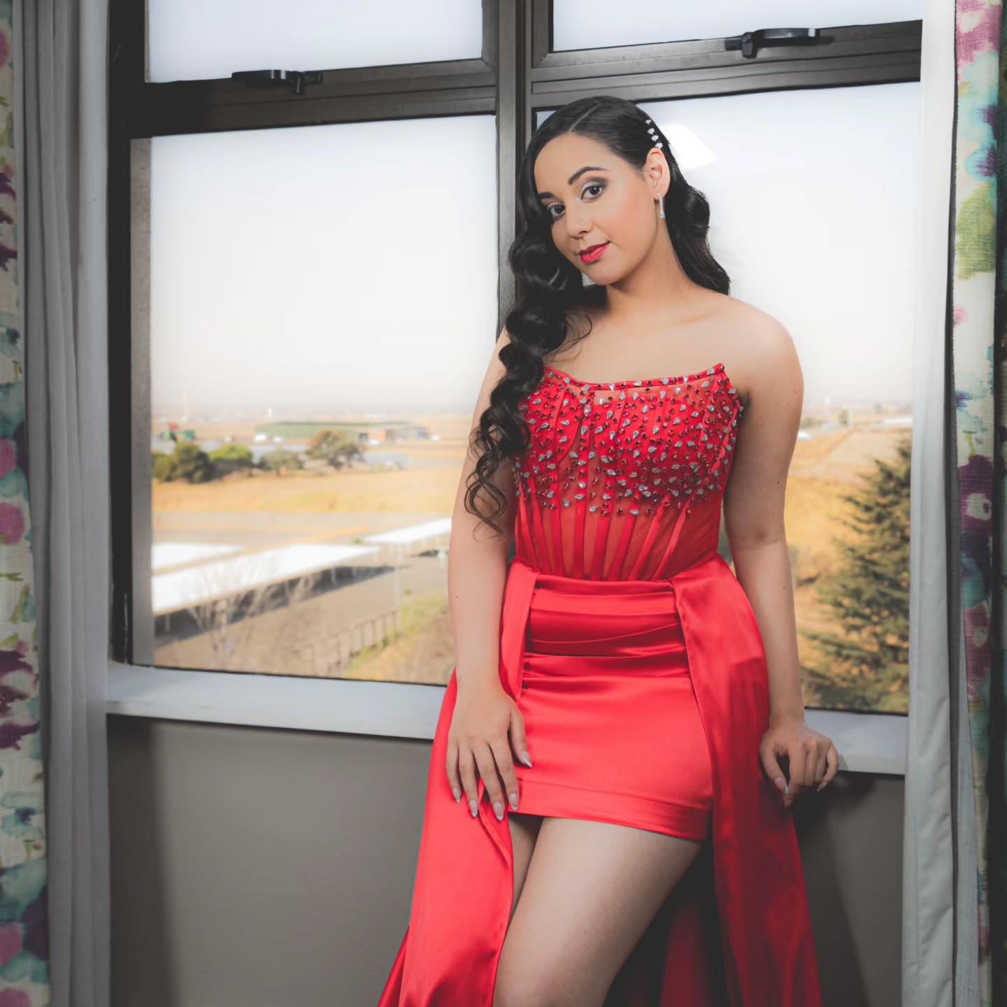Editorial portrait: model in a red gown posing in window light